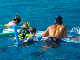 Mother, father, and their two sons floating on a surfboard.