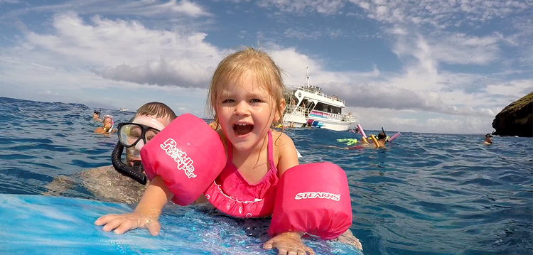 A toddler with pink floaties swimming with a parent.